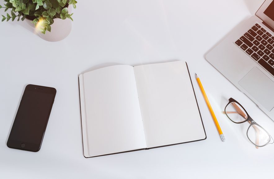 Open notebook, pencil and glasses on a white desk